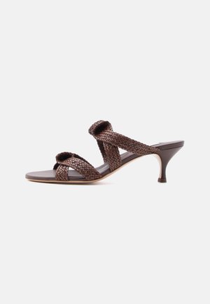 Ruskea kudottu nahkainen liukusandaali, jossa on kaksi remmiä ja matala korkokenkä, valkoisella taustalla.