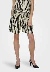 Beige shorts met een zwart zigzagpatroon, voorzien van een strikceintuur. Geweven stof, losse pasvorm, zijzakken, gecombineerd met zwarte hakken.