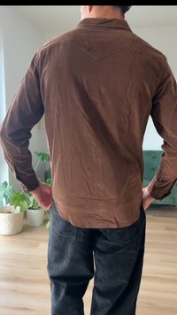 Bruine corduroy overhemd met een licht gestructureerde afwerking, met een puntig schouderstukontwerp aan de achterkant. Draagt met donkere corduroy broek.