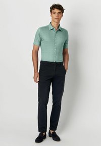 Muntgroene overhemd met korte mouwen en knopen, met een gestructureerde afwerking, gecombineerd met donkerblauwe broeken en donkerblauwe instappers.