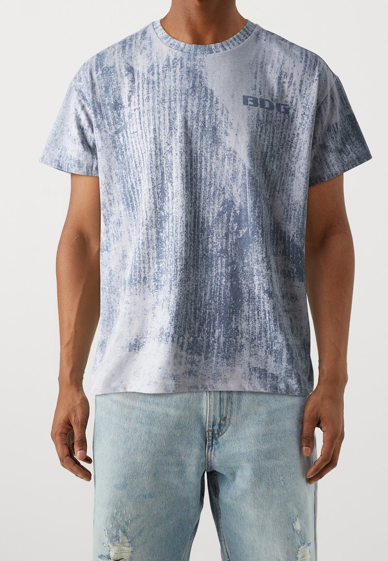 Krátký rukáv tričko v světle modré s texturovaným designem. Obsahuje malé logo na hrudi a kulatý výstřih. Materiál vypadá měkký.