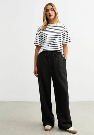T-shirt blanc à manches courtes avec des rayures horizontales noires, associé à un pantalon noir ample avec taille à cordon et revers.