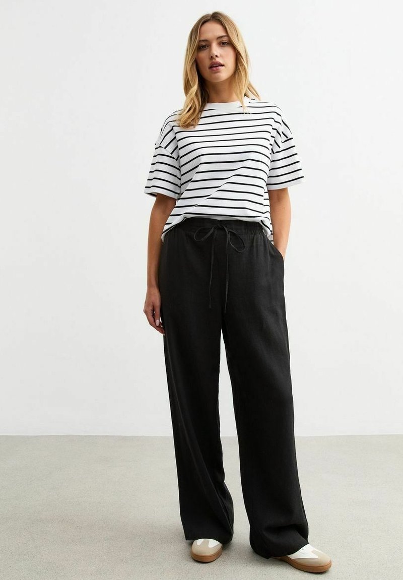 Witte t-shirt met korte mouwen en zwarte horizontale strepen, gecombineerd met losse zwarte broek met een trekkoord in de taille en opgerolde manchetten.