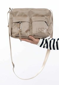 Borsa a tracolla beige con esterno texturizzato, due tasche frontali, hardware argentato e una lunga tracolla regolabile. Chiusura con cerniera sulla parte superiore.
