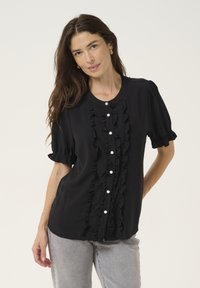 Schwarze Bluse mit kurzen Puffärmeln, verziert mit einem Rüschendetail auf der Vorderseite und perlenähnlichen Knöpfen, aus einem weichen, leichten Stoff gefertigt.