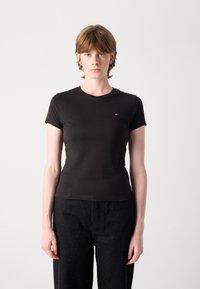 T-shirt noir ajusté à manches courtes, col rond et petit logo en rouge, blanc et bleu. Le matériau semble lisse et doux.