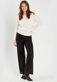 Pull blanc à manches longues associé à un pantalon large orné de sequins noirs et des bottes à talons noires.