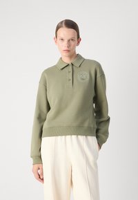 Olive zelený polokošeľový sveter s golierom, tromi gombíkmi a logom na hrudníku. Má voľný strih a rebrovaný lem a manžety.