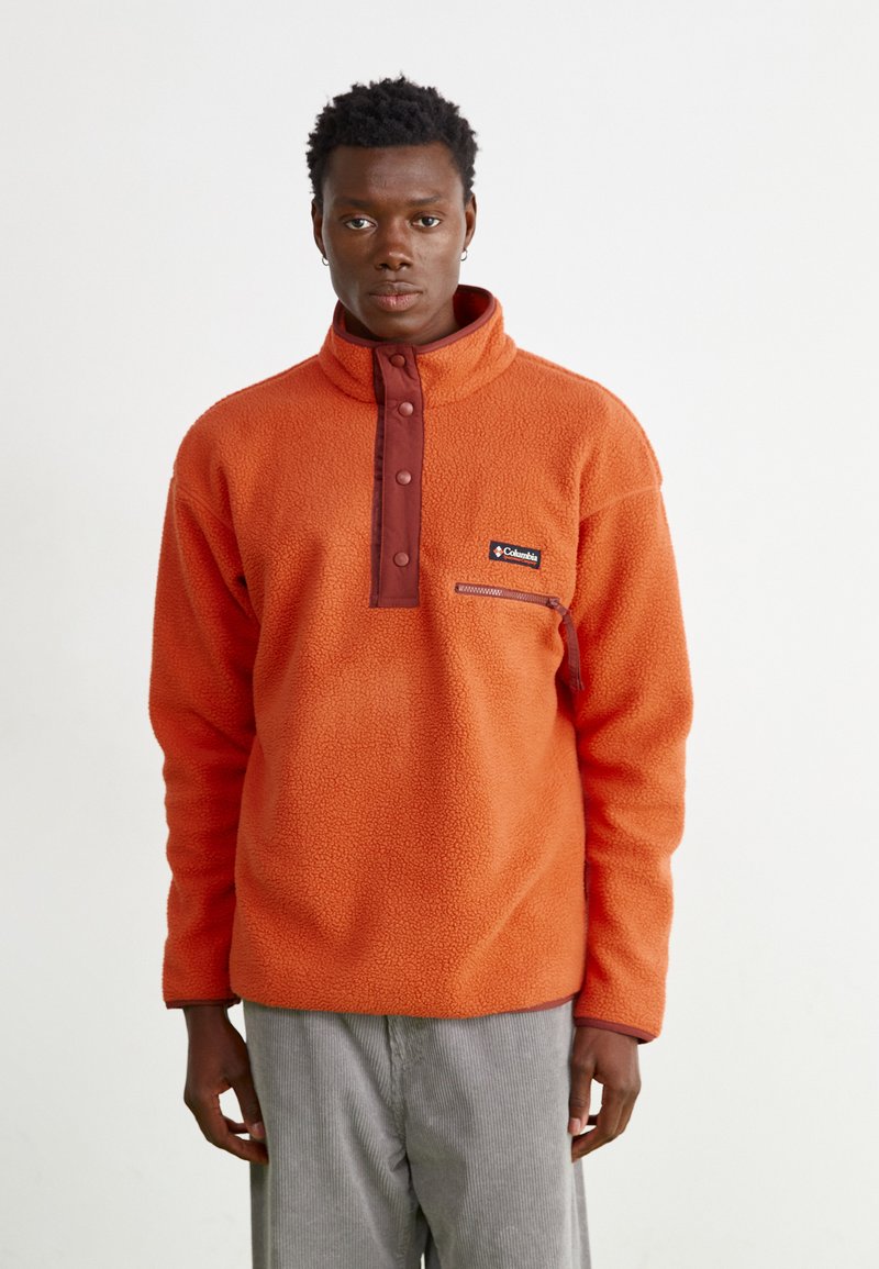 Oranje fleece pullover met hoge kraag, bruine knopenlijst en een rits borstzak; zachte textuur, relaxed fit.
