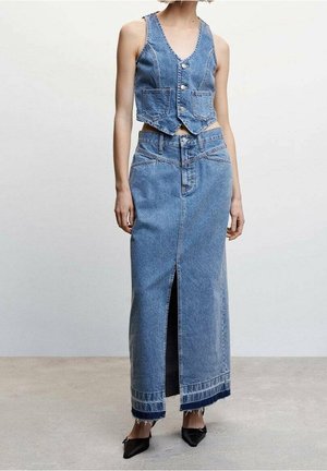 Kort denimvest met knoopsluiting en twee zakken, gecombineerd met een lange denimrok met een voorsplit en rafelige zoom. Zwarte schoenen.