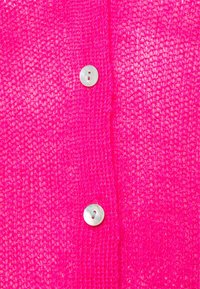 Tela de punto de color rosa brillante con un tejido texturizado, con un único botón blanco en el lado izquierdo.