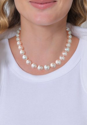 Collier de perles alternant des perles rondes crémeuses blanches et roses pâles sur un simple cordon, porté par-dessus un haut à côtes blanc.