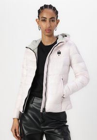 Giubbotto imbottito rosa chiaro con cappuccio grigio, zip frontale, due tasche laterali e una toppa con logo sul petto. Design trapuntato e testurizzato.