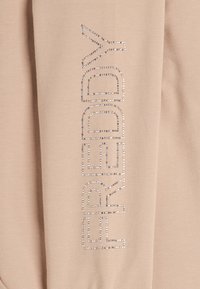 Felpa beige con la scritta "FREDDY" in strass, allineamento verticale. Tessuto morbido con una texture liscia, design minimalista.