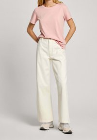 Ljusrosa bomull t-shirt i kombination med vida vita byxor. Skorna är ljusgrå och beige sneakers med snörning. Enkelt design.