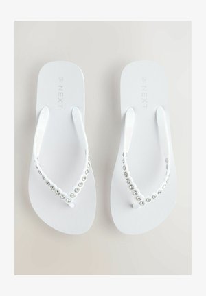 Balti šlepetės su tekstūruotu padu ir puošniu dirželiu, papuoštu skaidriais akmenimis. Dizainas apima lygų, išlenktą siluetą.