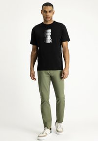 T-shirt nero a maniche corte con stampa grafica in grigio e bianco. Abbinato a pantaloni slim-fit verde oliva e sneakers bianche.