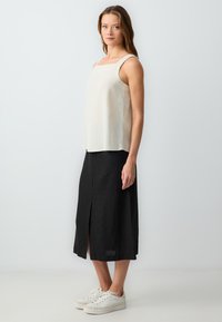 Helles beige ärmelloses Oberteil mit quadratischem Ausschnitt, kombiniert mit einem schwarzen Midikleid mit einem Schlitz vorne, getragen mit weißen Sneakers.
