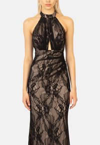 Abito da sera in pizzo nero con colletto halter alto, dettagli cut-out sul petto e silhouette aderente con sovrapposizione testurizzata.