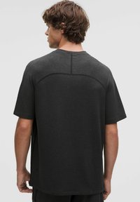 T-shirt nero a maniche corte con scollatura rotonda, spalle senza cuciture e texture liscia, mostrato da dietro.
