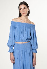 Blauw off-shoulder cropped top met elastische smocking en lange, opgeblazen mouwen. Geborduurde bloemdetails door het geheel. Lichte stof.