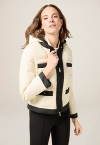 Padded jacket in cream and black, featuring a zip front, hood, and four front pockets with contrasting black details and trim.