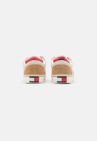 Sneakers beige e tan con accenti rosa, toppe in suede sul tallone e suole bianche. Il marchio sul retro presenta blocchi di colore rosso, bianco e blu.
