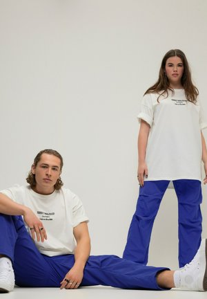 Hvide oversized t-shirts med sort tekst, parret med blå cargo bukser. Outfitsne har minimalistisk design og en afslappet pasform.
