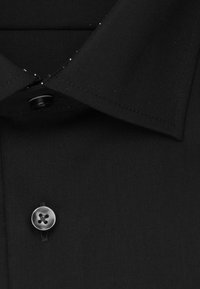 Zwart shirt met een spitse kraag, enkele zwart knoopsluiting en een gladde stoftextuur. Bevat fijne stikdetails.