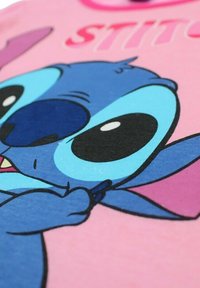 T-shirt rose présentant un grand personnage de dessin animé bleu avec de grands yeux, des détails faciaux complexes et une expression accentuée.