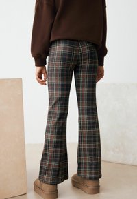 Pantaloni a zampa d'elefante in plaid nero, rosso e bianco, con un motivo a quadri e una texture di tessuto liscia, abbinati a stivaletti marroni alla caviglia.