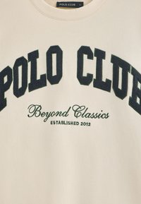 Felpa crema con "POLO CLUB" stampato in lettere verdi scure e testurizzate. Presenta "Beyond Classics" e "ESTABLISHED 2012" in testo verde più piccolo.