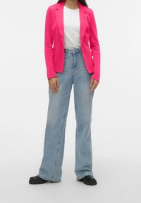 Blazer fucsia, t-shirt bianca, jeans a gamba larga blu chiaro e scarpe nere. Il blazer presenta un bottone singolo e due tasche frontali.