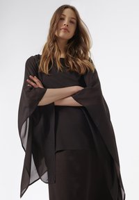 Schwarzes geschichtetes Kleid mit durchsichtigen, fließenden Ärmeln. Der Stoff wirkt leicht und glatt, mit einem runden Ausschnitt und lockerer Passform.