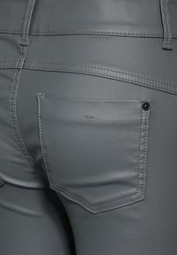 Gros plan sur un pantalon en cuir gris montrant des coutures détaillées, une poche arrière avec rivet, et des passants de ceinture.