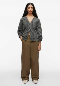 Grijs denimjack met een V-hals, twee borstzakken en knoopsluiting, gecombineerd met bruine wijde broek en beige schoenen.