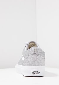 Chaussure à paillettes argentées avec une forme arrondie, des accents blancs, une tige texturée et un détail de logo sur le talon. Conception standard de semelle plate.