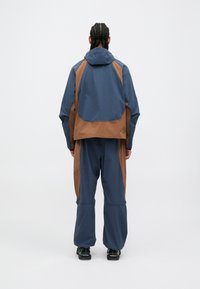 Αδιάβροχο μπουφάν και παντελόνι σε σχέδιο μπλοκ χρωμάτων ναυτικού μπλε και καφέ. Διαθέτει κουκούλα, άνετη εφαρμογή και ανθεκτικό ύφασμα.