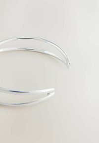 Culoare metalică argintie, cercel de ureche cu un finisaj neted și lustruit, având un design minimalist. Forma este curbată, asemănătoare cu o bandă subțire.