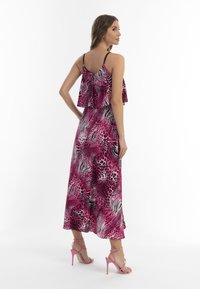Rochie maxi cu imprimeu animal în nuanțe de roz și negru, cu un top cu volane în straturi, bretele spaghetti și tivul despicat, asortată cu sandale roz cu toc înalt.