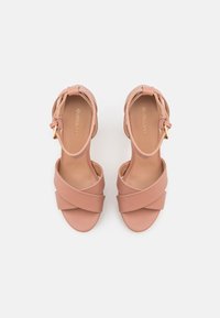 Sandales roses à lanières avec des bandes en tissu croisées et une bride de cheville dotée d'une boucle en ton doré. Texture lisse et design à bout ouvert.