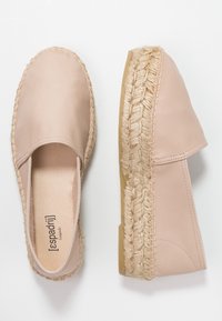 Espadrilles beige hechas de cuero suave con suela de cuerda de yute. Diseño de punta cerrada con acentos cosidos a lo largo de los bordes.