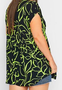 Maglietta nera con stampa di foglie verde neon, maniche corte e vestibilità ampia. Il tessuto è leggero, con una consistenza morbida e dettagli arricciati in vita.