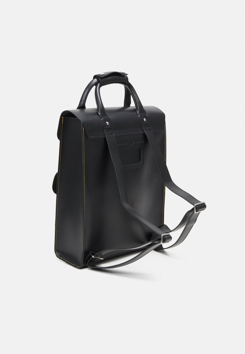 Sort læderrygsæk med gule syninger, dobbelte håndtag og justerbare skulderremme. Har en baglomme og en struktureret design.