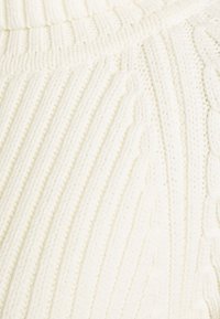 Flauschiger Strickpullover in Off-White, mit erhabenen Rippmustern und subtilen Kabeldetails. Weiche Textur mit einem entspannten, gemütlichen Erscheinungsbild.
