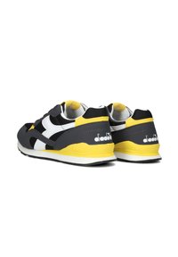 Sneaker neri, grigi e bianchi con dettagli gialli, caratterizzati da una tomaia testurizzata e una suola imbottita. Include logo laterale e design elegante.