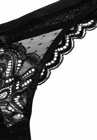 Zwarte kant slip met doorschijnende mesh panelen, bloemenkant afwerking, gekartelde randen en een gladde tailleband. Delicaat geconfigureerd detail.