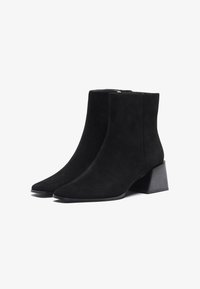 Botas de tobillo de ante negro con punta afilada y tacón bloque de altura media. Textura suave, diseño minimalista y silueta elegante.