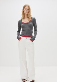 Tricou gri cu mânecă lungă și detalii roșii, asortat cu pantaloni albi cu picioare largi. Ținuta are o croială confortabilă și o textură netedă, având buzunare laterale.