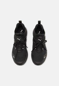 Baskets de sport noires avec une tige en mesh, surface texturée, design à lacets, et un logo Puma blanc sur le côté et la languette.